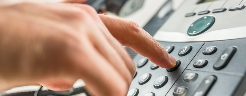 A person pressing a button on a telephone.