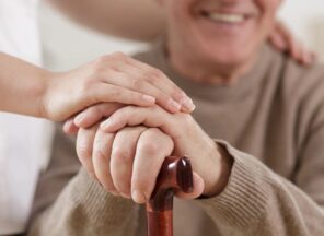 An elderly man is holding the hand of a caregiver.
