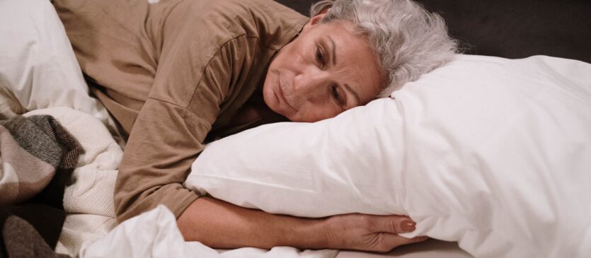 Older woman lying with head on pillow.